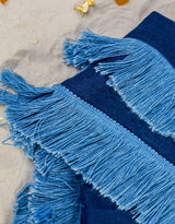 Riviera Blanket is made of linen in navy blue, its soft double-sided design adorned with a fun cotton fringe in a lighter shade of blue, creating a beautiful tone-in-tone effect.