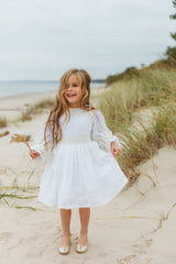 Exquisite soft linen knee-length beach dress with majestic cotton lace details, bishop sleeves, a self-tie belt, and a covered button fastening in the back.