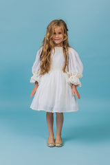 Exquisite soft linen knee-length beach dress with majestic cotton lace details, bishop sleeves, a self-tie belt, and a covered button fastening in the back.