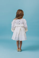 Exquisite soft linen knee-length beach dress with majestic cotton lace details, bishop sleeves, a self-tie belt, and a covered button fastening in the back.