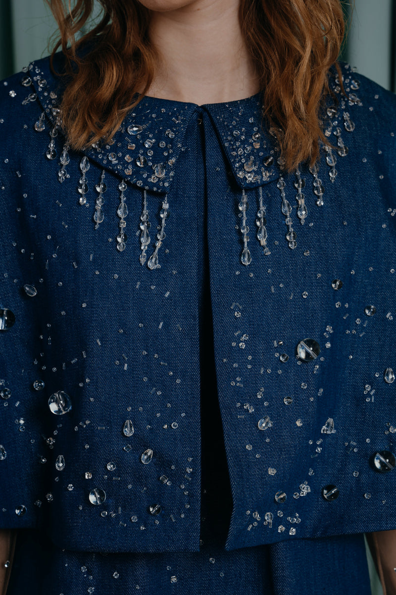 Short soft and breathable denim cape with intricate crystal and transparent resin pearl detailing creates a beautiful and eye-catching pattern that shimmers in the light. Short soft and breathable denim cape