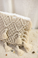 Riviera Square Cushion is made of linen in ivory white and adorned with a hand-knotted macramé in a natural shade. 