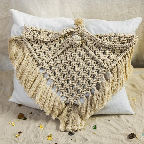 The Riviera Triangle Cushion is made of linen in ivory white and adorned with a hand-knotted macramé in a natural shade.