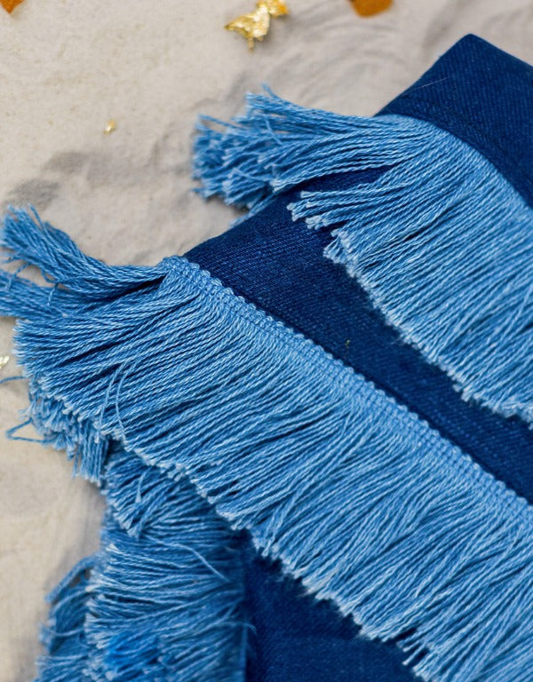Riviera Blanket is made of linen in navy blue, its soft double-sided design adorned with a fun cotton fringe in a lighter shade of blue, creating a beautiful tone-in-tone effect.