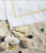 The Riviera Blanket is made of linen in foggy white, its soft double-sided design adorned with hand-made tassels and pom-poms.