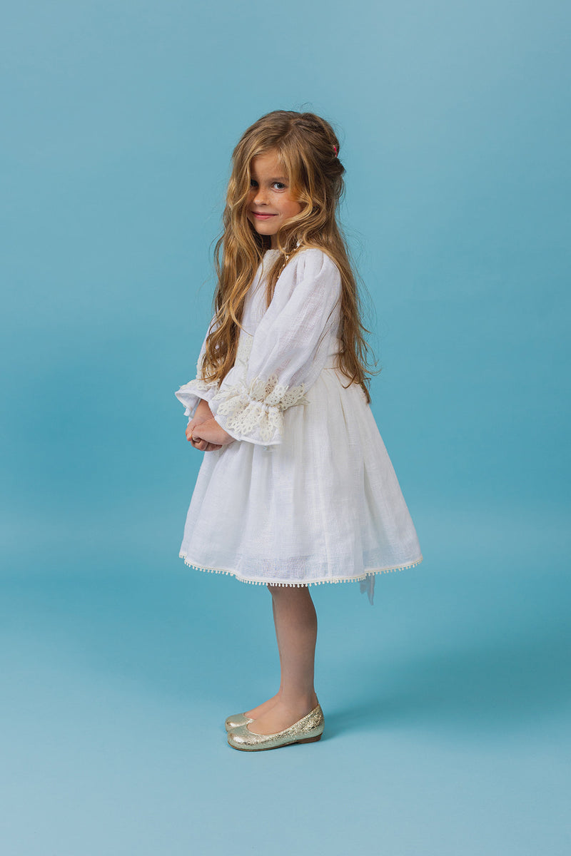Exquisite soft linen knee-length beach dress with majestic cotton lace details, bishop sleeves, a self-tie belt, and a covered button fastening in the back.